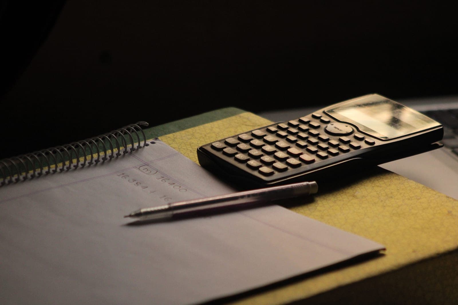 A calculator and notebook on a desk, mid-calculation